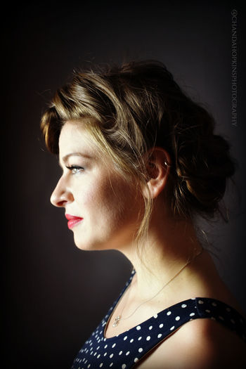 Profile shot of a woman with an updo and ear piercing looks into the light.
