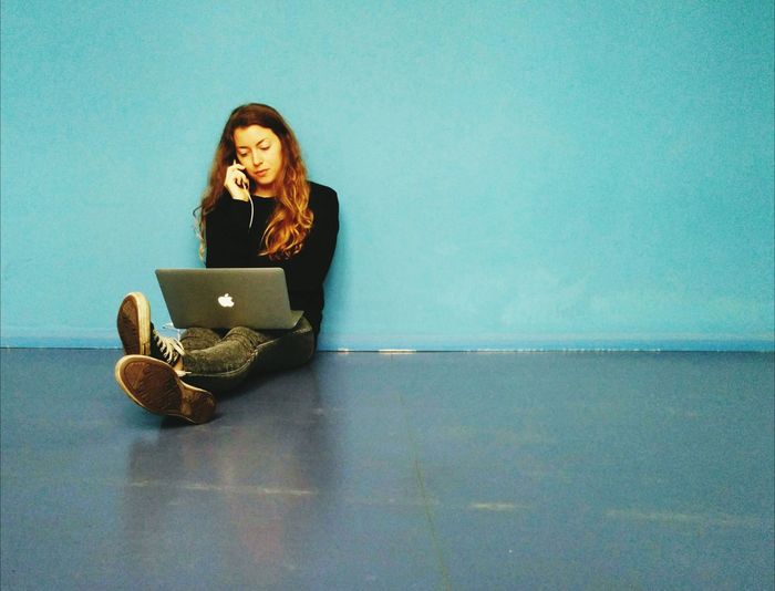 Young woman talking on phone while sitting on floor with laptop