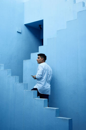 Side view of young man looking away while standing on staircase against wall