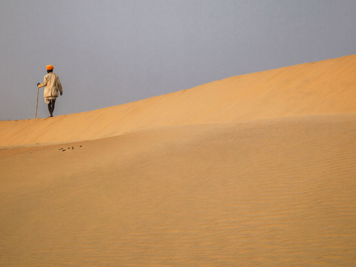 Rear view of man on sand dune in desert against sky