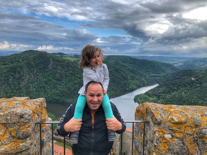 Portrait of smiling man carrying daughter on shoulders against mountains