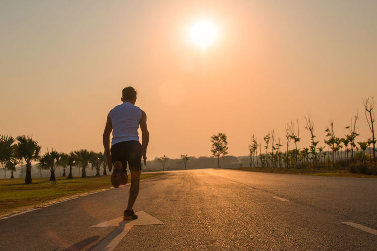 Rear view of man running on road against sky during sunset