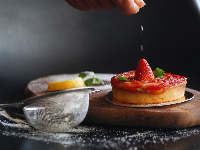Cropped image of hand sprinkling sugar on strawberry tart
