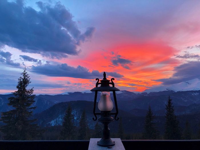 Single outdoor lamp on the terrace during beautiful orange sunset surrounded by evergreen trees