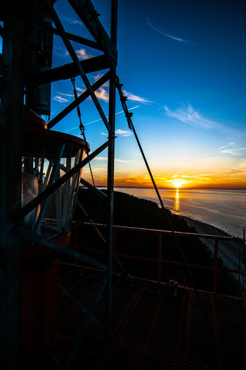 Silhouette railing by sea against sky during sunset