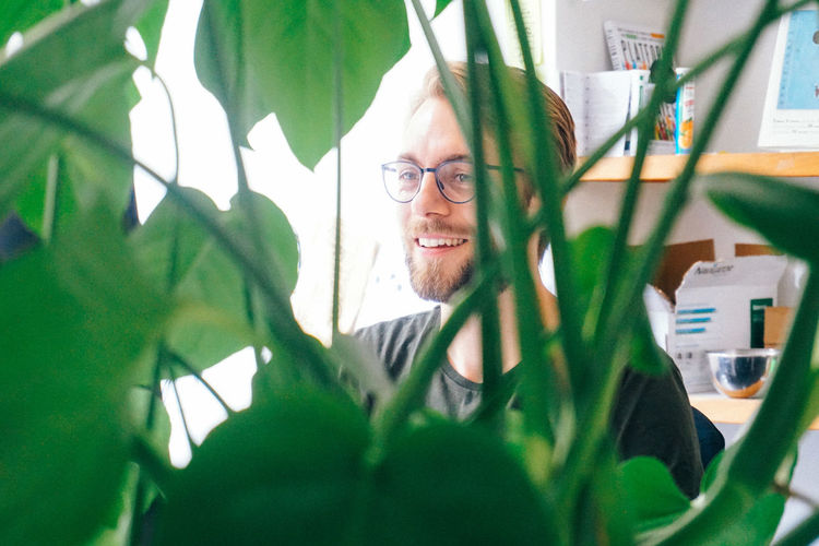Smiling young man seen through plants in office