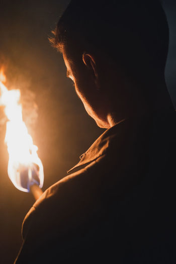 Midsection of man holding lit candle in the dark