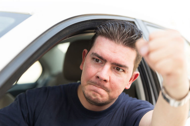 Frustrated man gesturing through window while traveling in car
