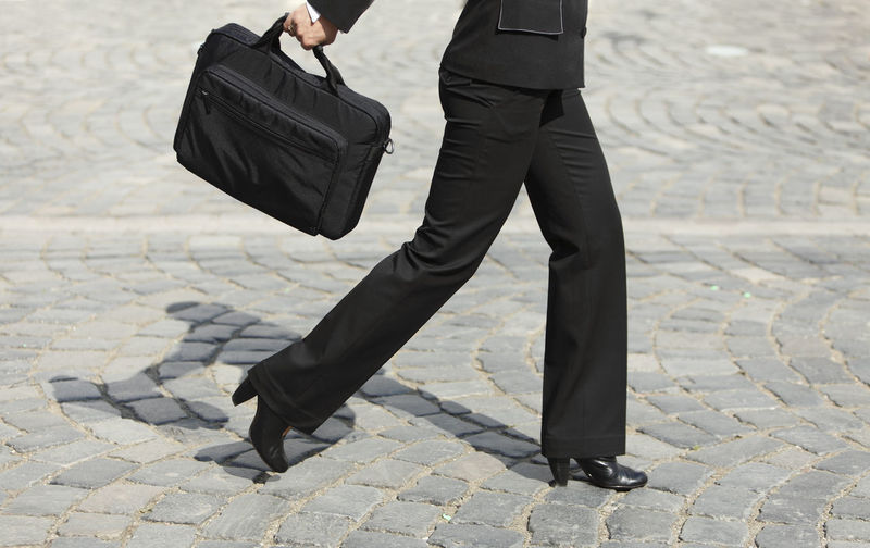 Low section of businesswoman holding bag while walking on city street