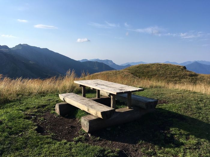 Bench on field by mountains against sky