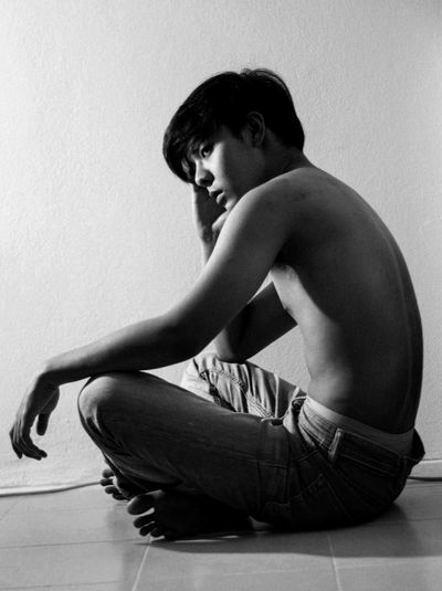 Shirtless young man sitting against wall at home