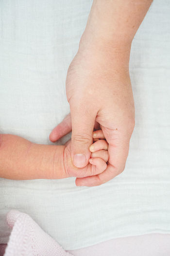 Close-up of infant and adult holding hands on bed