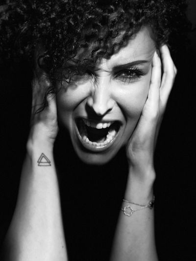 Close-up portrait of woman shouting against black background