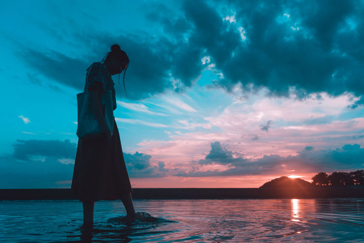 Silhouette woman standing by swimming pool against sky during sunset