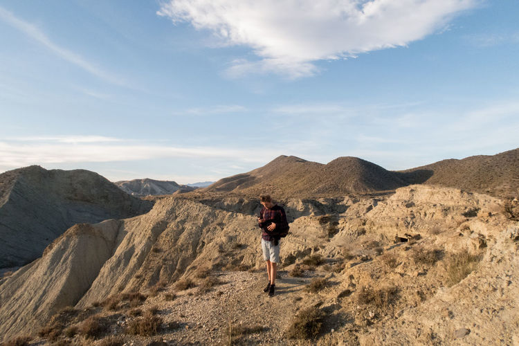 Man using mobile phone while standing on mountain against sky
