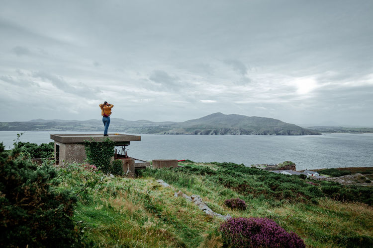Woman standing by sea against cloudy sky