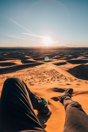 Low section of people relaxing on land against sky during sunset