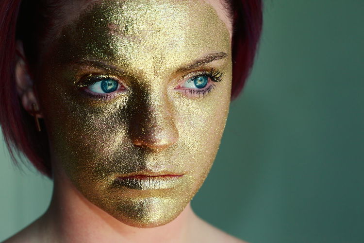 Close-up of woman face with golden paint against green background
