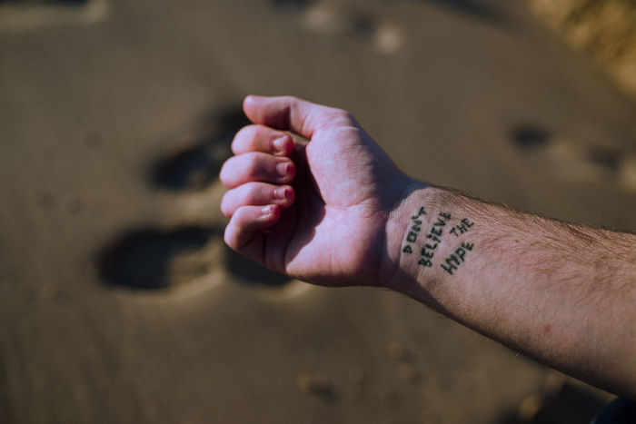 Cropped hand of man with tattoo at sandy beach