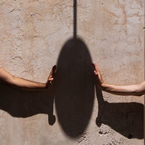 Cropped image of hands by shadow against wall