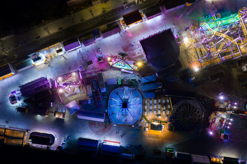 Drone view of public amusement park with various bright glowing attractions located on dark street of city at night time