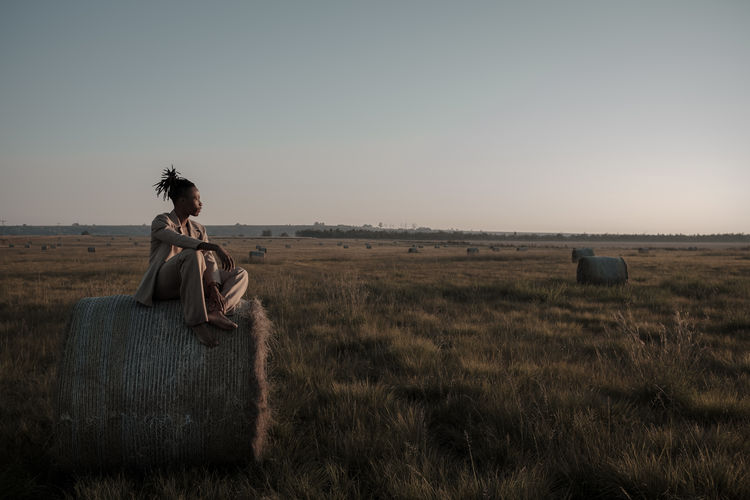 Young man sitting on hay bale at agricultural landscape