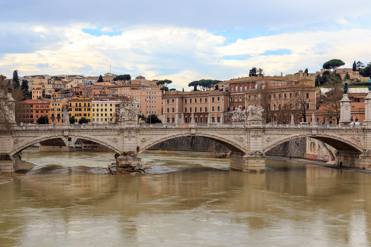 Arch bridge over river in city against sky