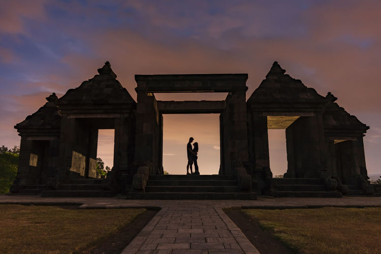 A couple standing at historic building against sky during sunset