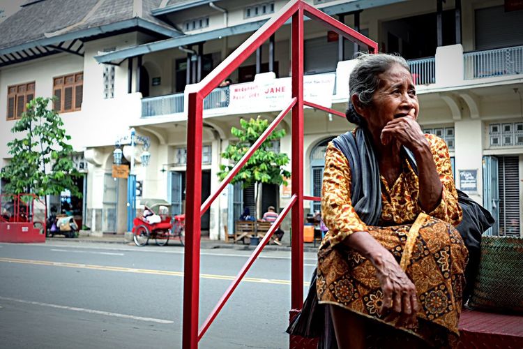 Senior woman sitting on steps against street