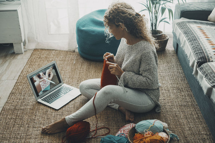 Rear view of woman using laptop while sitting on sofa at home