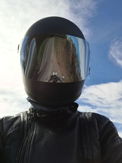 Man wearing helmet with reflection of motor cycle against sky