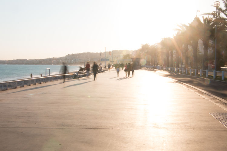 People walking on footpath by sea against clear sky