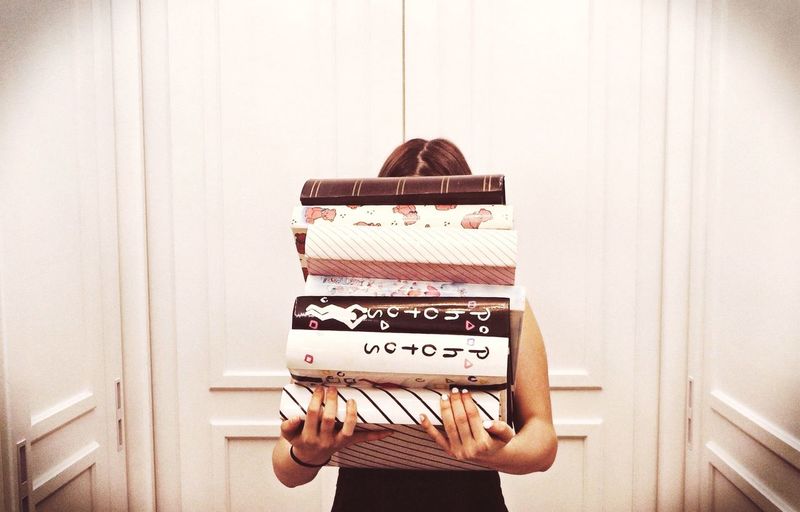 Woman holding stack of books against wall