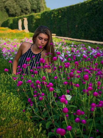 Young woman sitting amidst with pink flowers on field