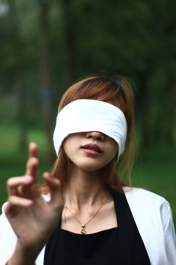 Beautiful young woman with blindfold against trees