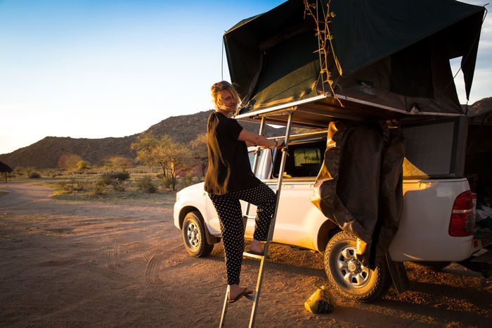 Portrait of woman standing on tent ladder by pick-up truck at desert