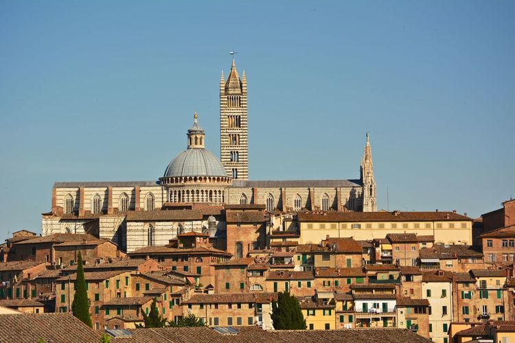 Buildings and duomo di siena against blue sky