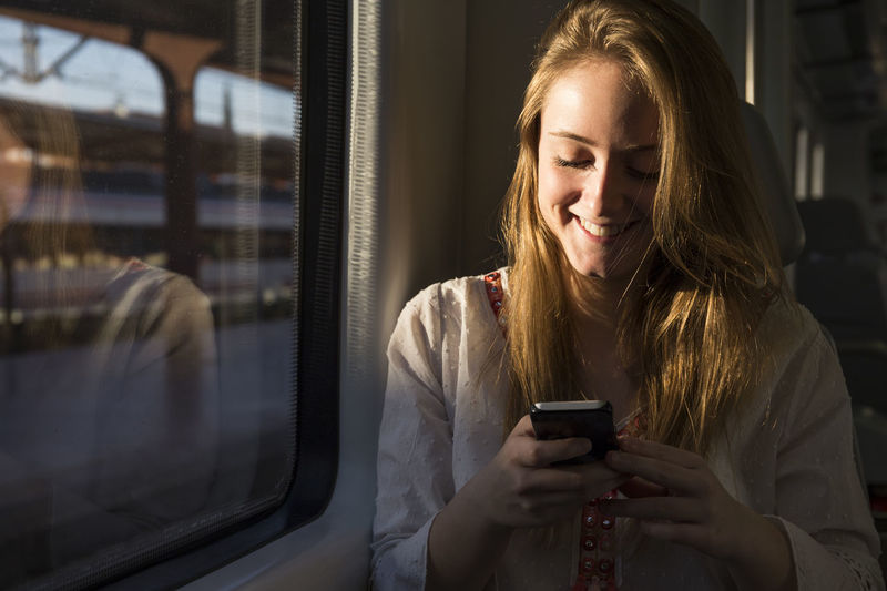 Smiling young woman on a train looking at cell phone