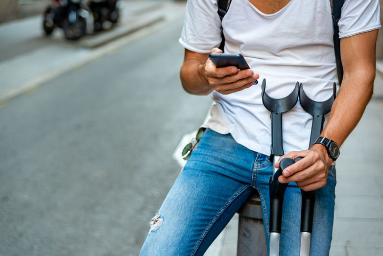 Unrecognizable young man with crutches and mobile in the street
