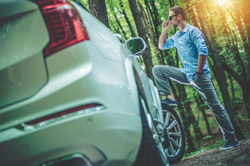 Side view of man standing by car in forest
