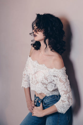 Girl with black hair curled in curls, turned sideways, wearing a lace white top and tight jeans