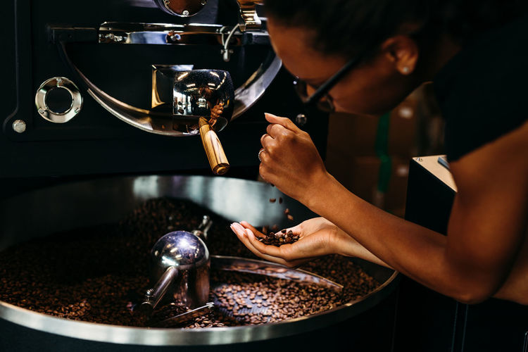 Close-up of woman with roasted coffee beans in machinery at cafe