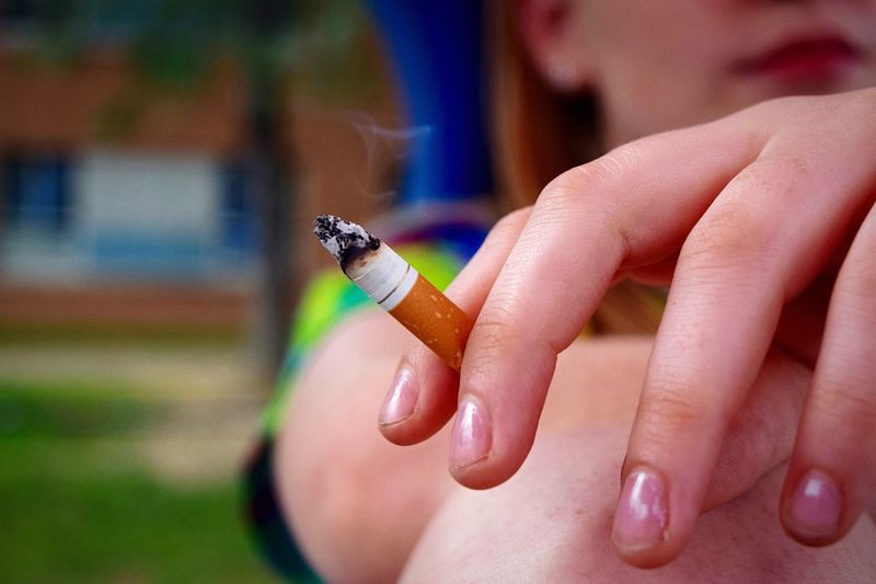 Cropped image of woman hand holding cigarette at park