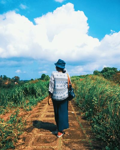 Rear view of woman walking on field against sky