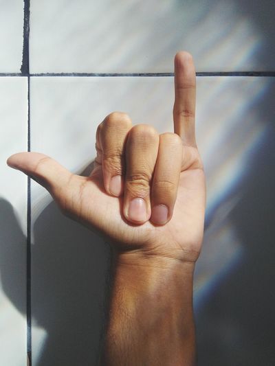 Cropped hand showing shaka sign by wall