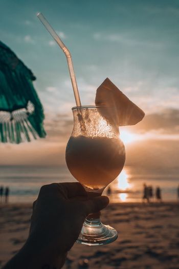Cropped hand having drink at beach during sunset