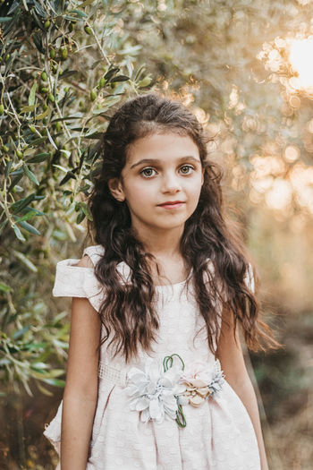 Portrait of little girl standing against tree