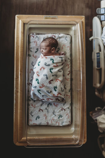 Overhead view of newborn baby boy in hospital bassinet with blankets