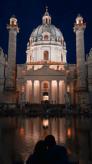 People with reflecting pool in background against illuminated church at night
