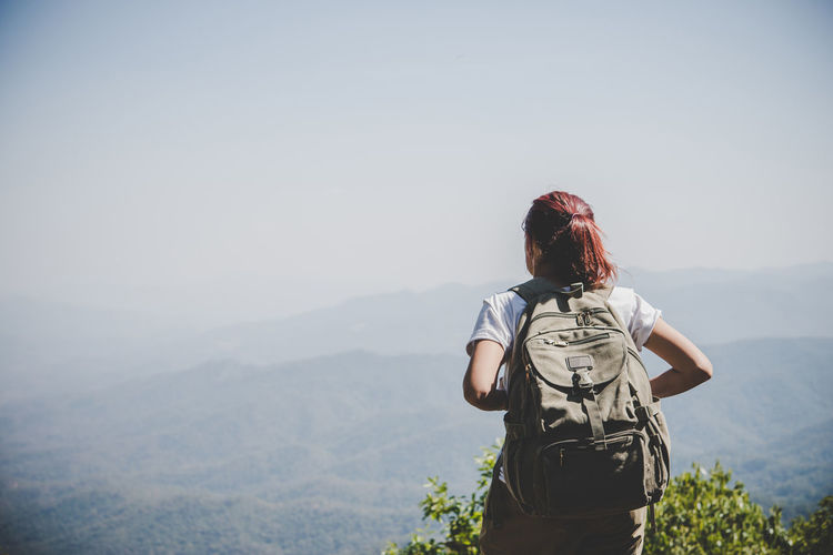 Rear view of backpack woman looking at mountains against sky